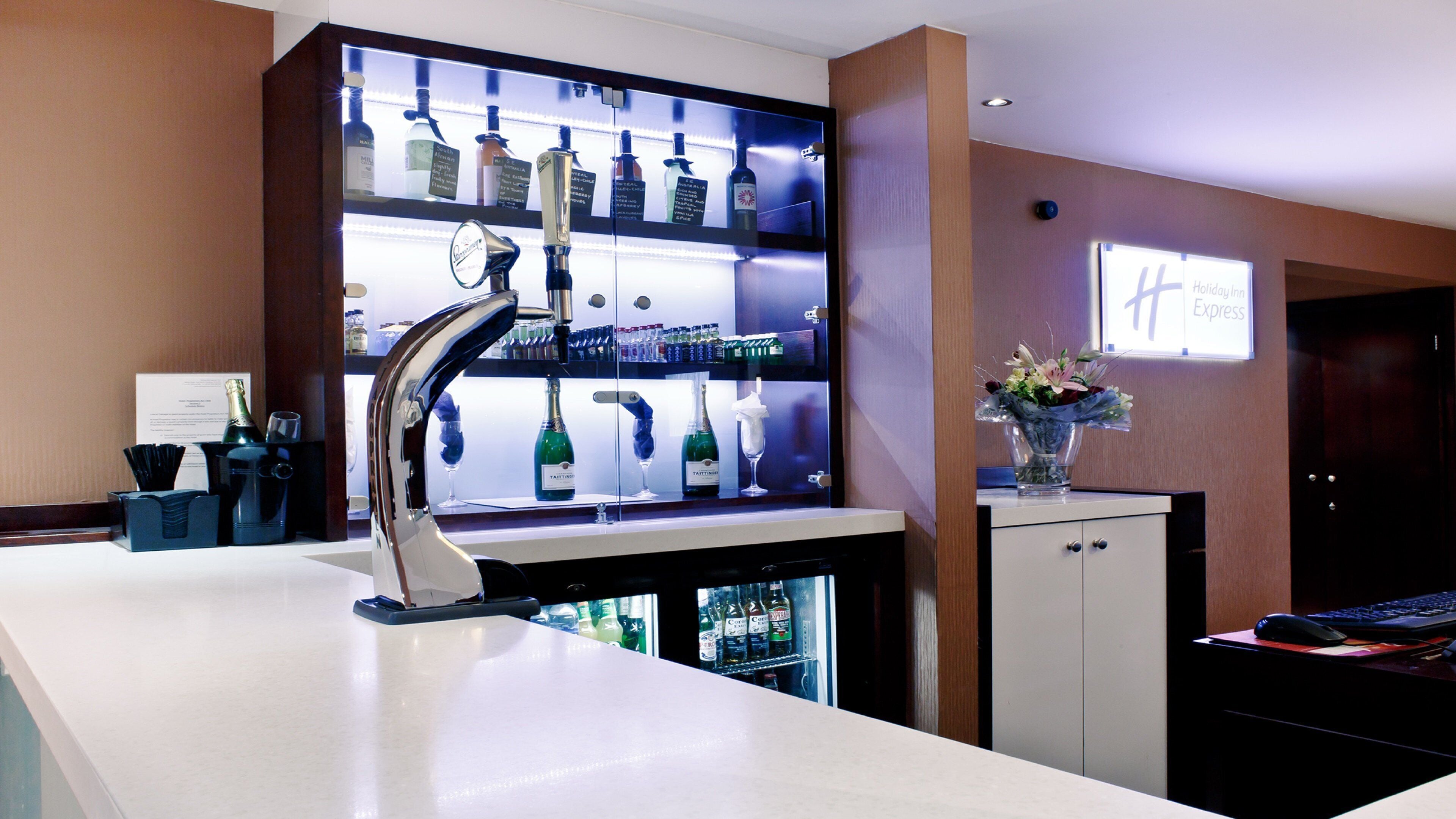 Een hotel receptie met een bar, een minibar en een digitaal scherm.