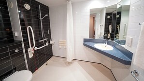 A modern bathroom with a black and white tiled shower area, a white toilet, and a blue countertop sink with a large mirror. - Holiday Inn Express Leeds East by IHG (Leeds)