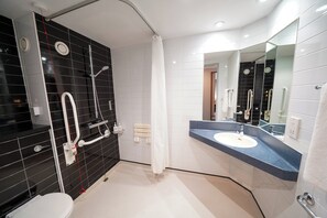 A modern bathroom with a black and white tiled shower area, a white toilet, and a blue countertop sink with a large mirror. - Holiday Inn Express Leeds East by IHG (Leeds)