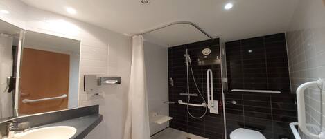 Un baño moderno con un lavamanos blanco, un inodoro, una ducha con cabezal de ducha de mano y un espejo con toallero.