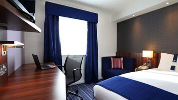 Una camera d'albergo con un letto, una scrivania, una sedia e una finestra con tende.