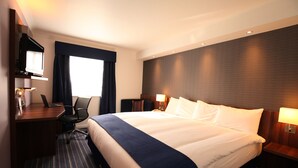A hotel room with a large bed, a desk with a laptop, a television, and a window with curtains. - Holiday Inn Express Leeds East by IHG (Leeds)