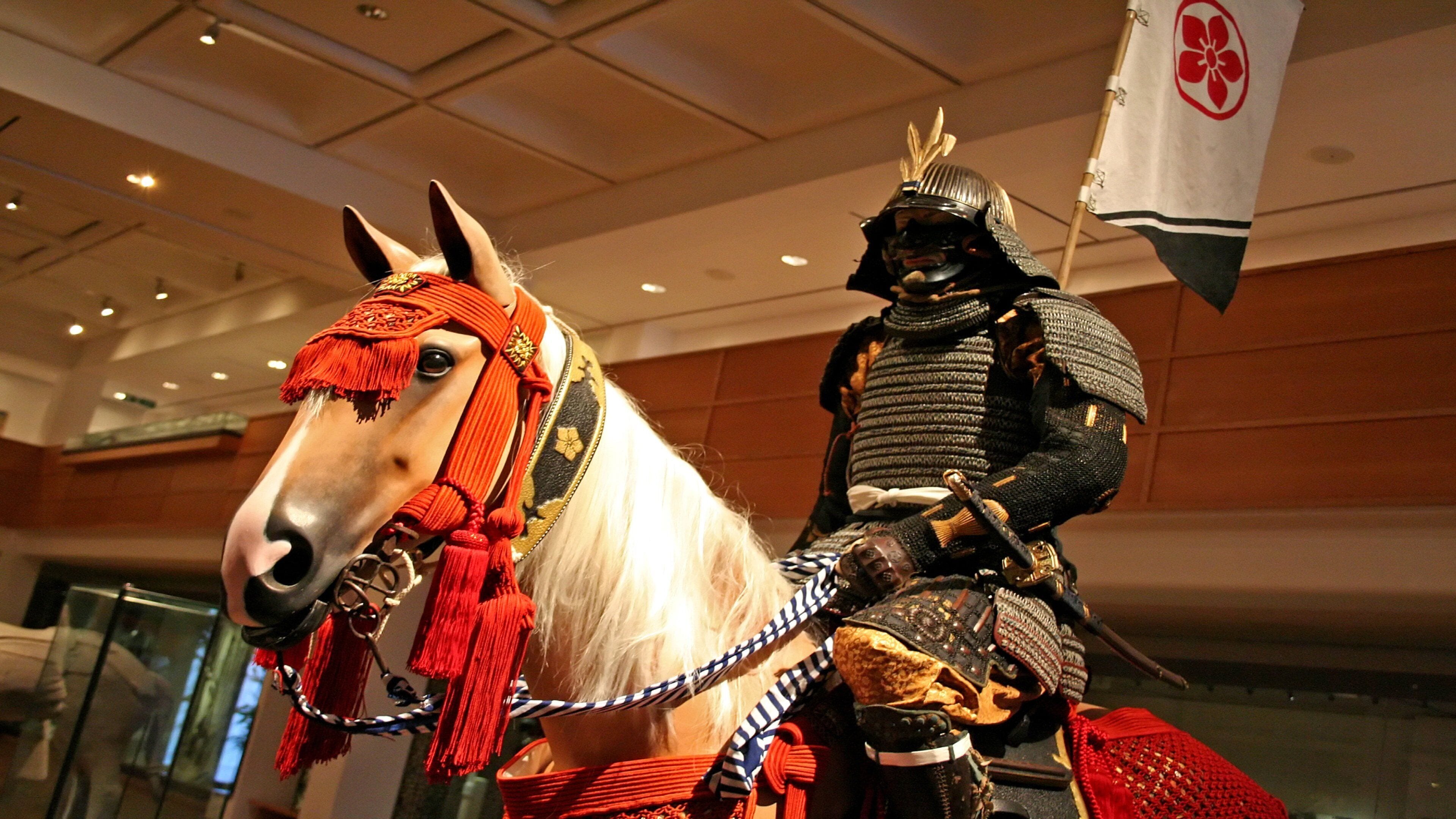 A horse with a rider in traditional armor, both indoors with a ceiling and walls visible.
