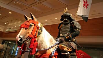 A horse with a rider in traditional armor, both indoors with a ceiling and walls visible.