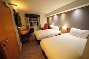 Habitación de hotel con dos camas, un escritorio, una silla, un televisor y una ventana con cortinas.