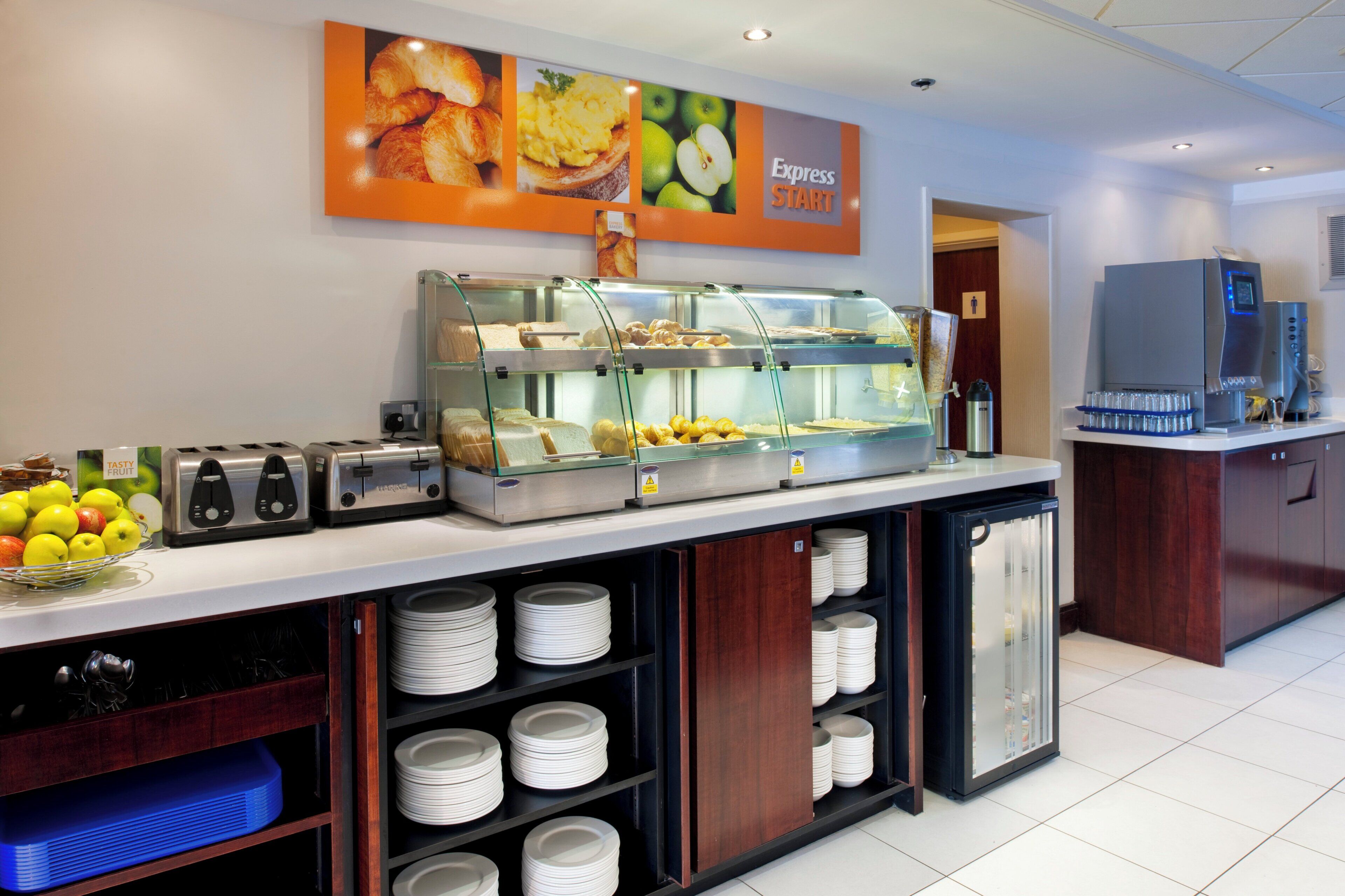Zona de desayuno tipo buffet con vitrina de vidrio, tostadora y un cartel anunciando 'Express START'.
