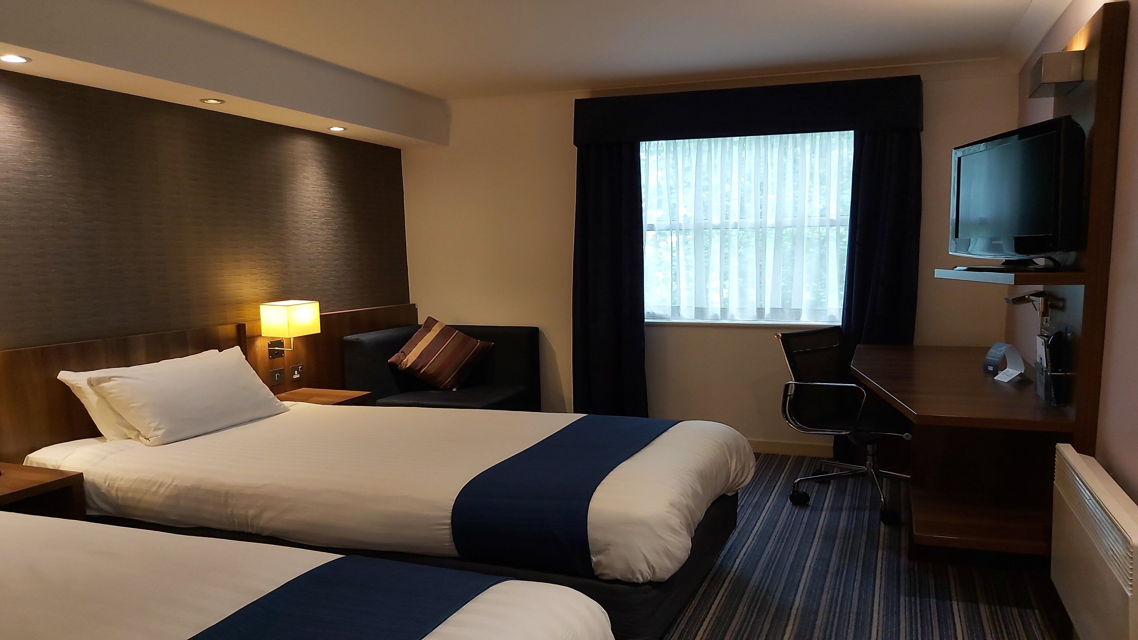A hotel room with two beds, a desk, a chair, a television, and a window with curtains.