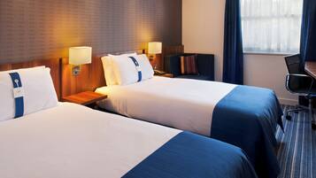 A hotel room with two beds, bedside tables, lamps, a desk, and a chair.
