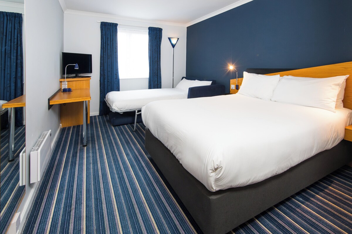Una habitación de hotel con una cama grande, dos camas más pequeñas, un escritorio con una computadora y un televisor.