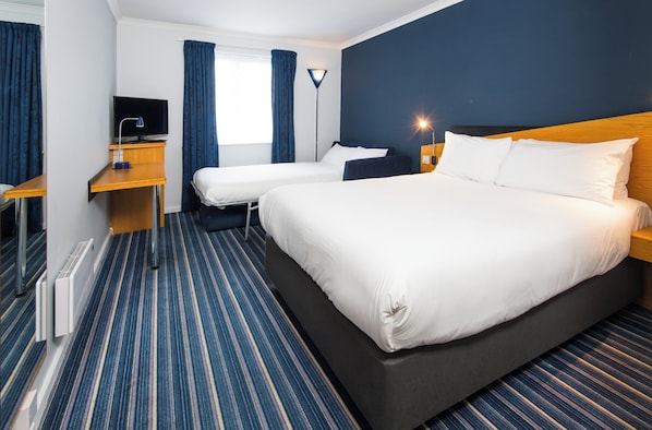 Una habitación de hotel con una cama grande, dos camas más pequeñas, un escritorio con una computadora y un televisor.