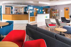 Un hall de hotel con mostrador de recepción, zona de estar y máquina expendedora.