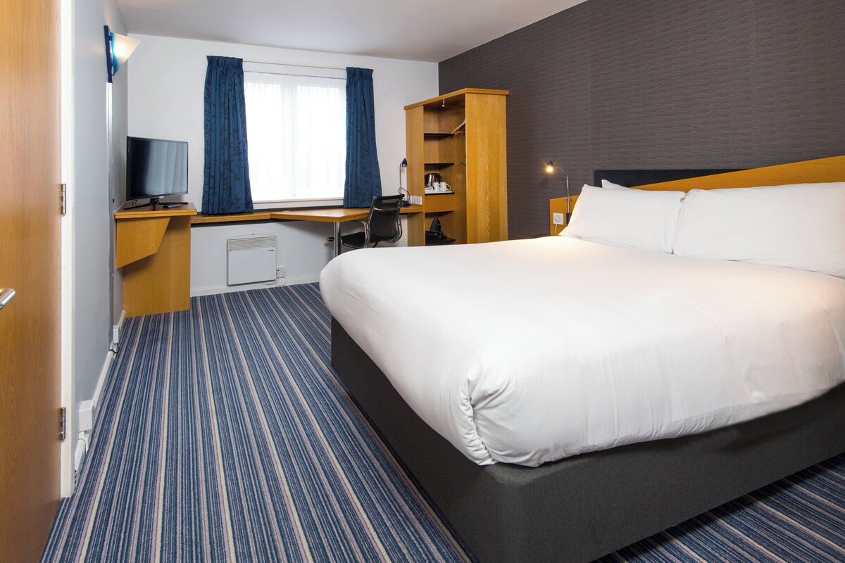 Una habitación de hotel con una cama grande, un escritorio con una computadora, un televisor y un armario.