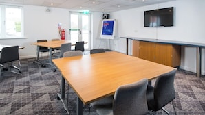 A conference room with a large table, chairs, a whiteboard, a fire extinguisher, and a television on the wall. - Holiday Inn Express Manchester East by IHG (Manchester)