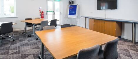 A conference room with a large table, chairs, a whiteboard, a fire extinguisher, and a television on the wall.