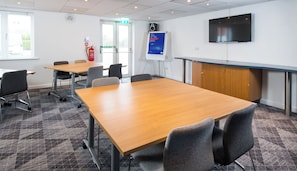 A conference room with a large table, chairs, a whiteboard, a fire extinguisher, and a television on the wall. - Holiday Inn Express Manchester East by IHG (Manchester)