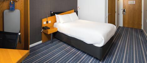 A hotel room with a bed, bedside table, and a desk with a chair.