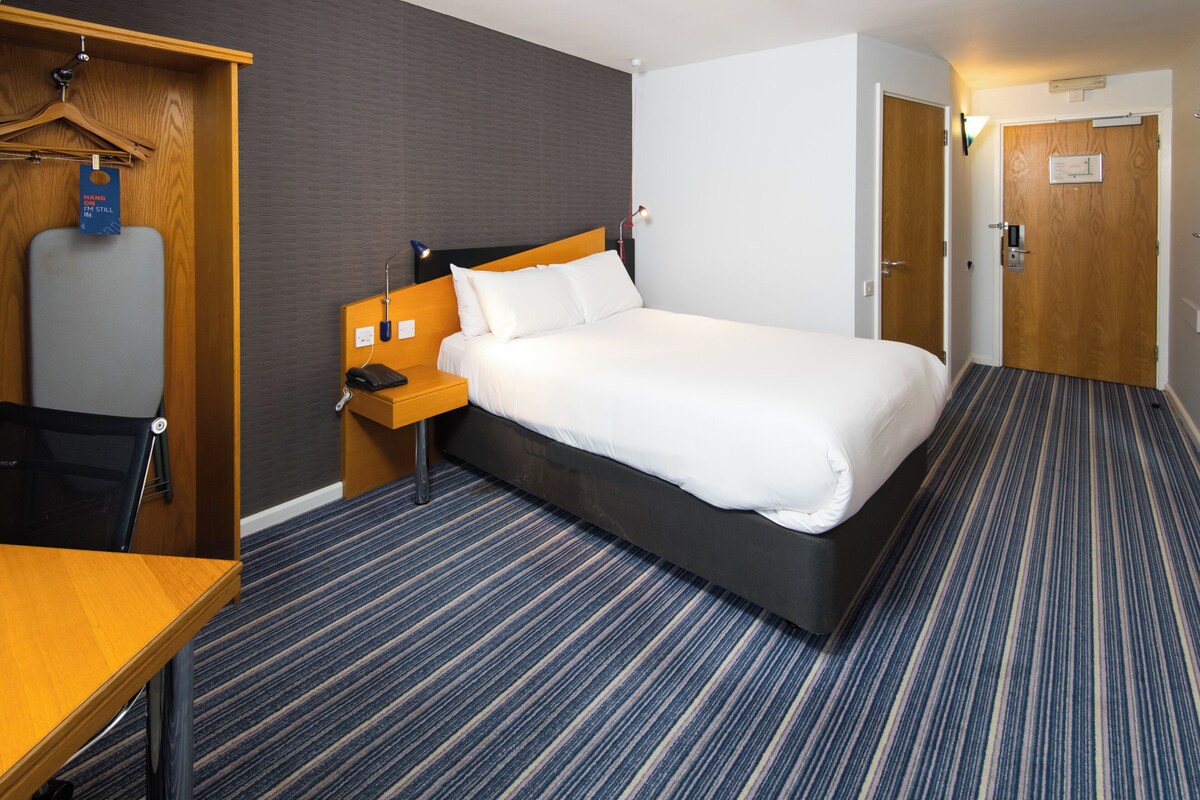 Una habitación de hotel con cama, escritorio de madera, silla, armario y puerta.