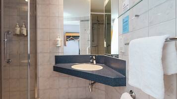 A modern bathroom with a glass shower enclosure, a sink with a dark countertop, and a towel rack with a white towel.