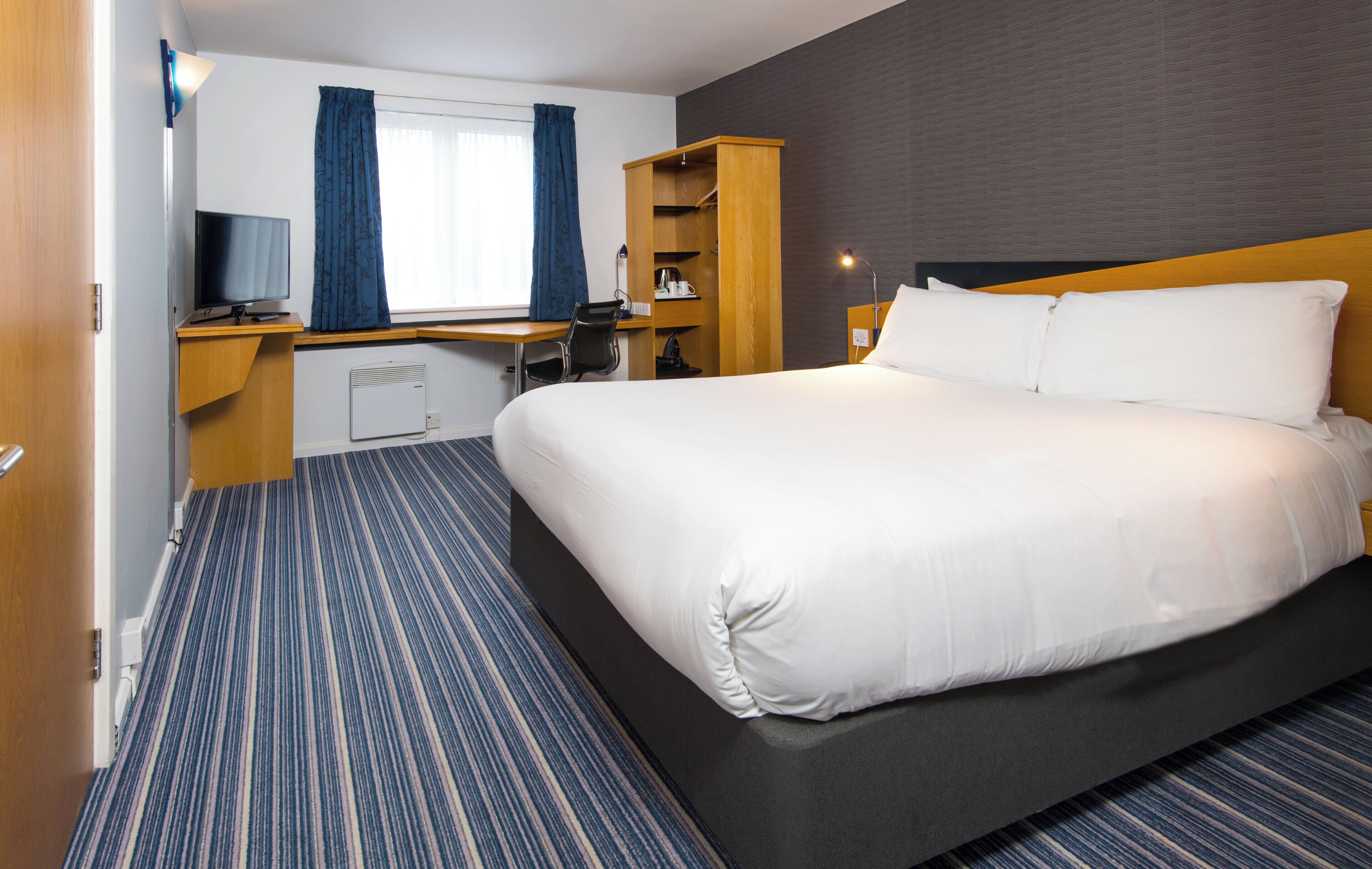 Een hotelkamer met een groot bed, een bureau met een computer, een stoel, een televisie en een kledingkast.