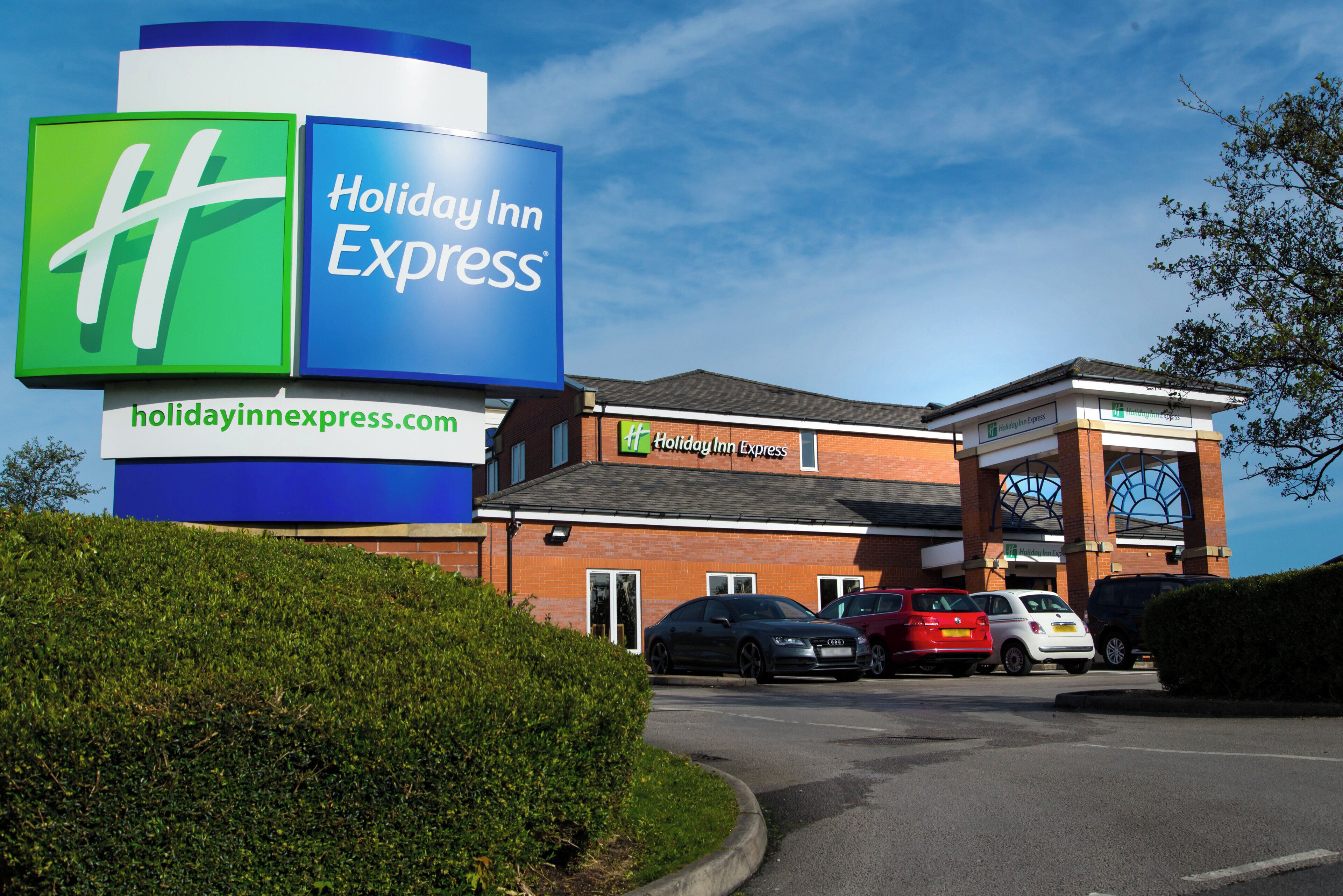 A Holiday Inn Express hotel with a prominent sign, a parking lot, and a brick building facade.