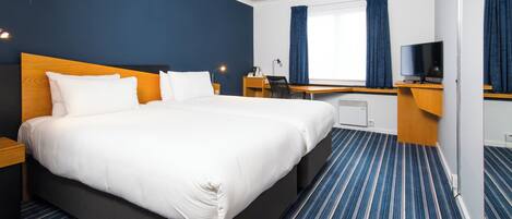 A hotel room with a large bed, a desk, a chair, a television, and a window with curtains.