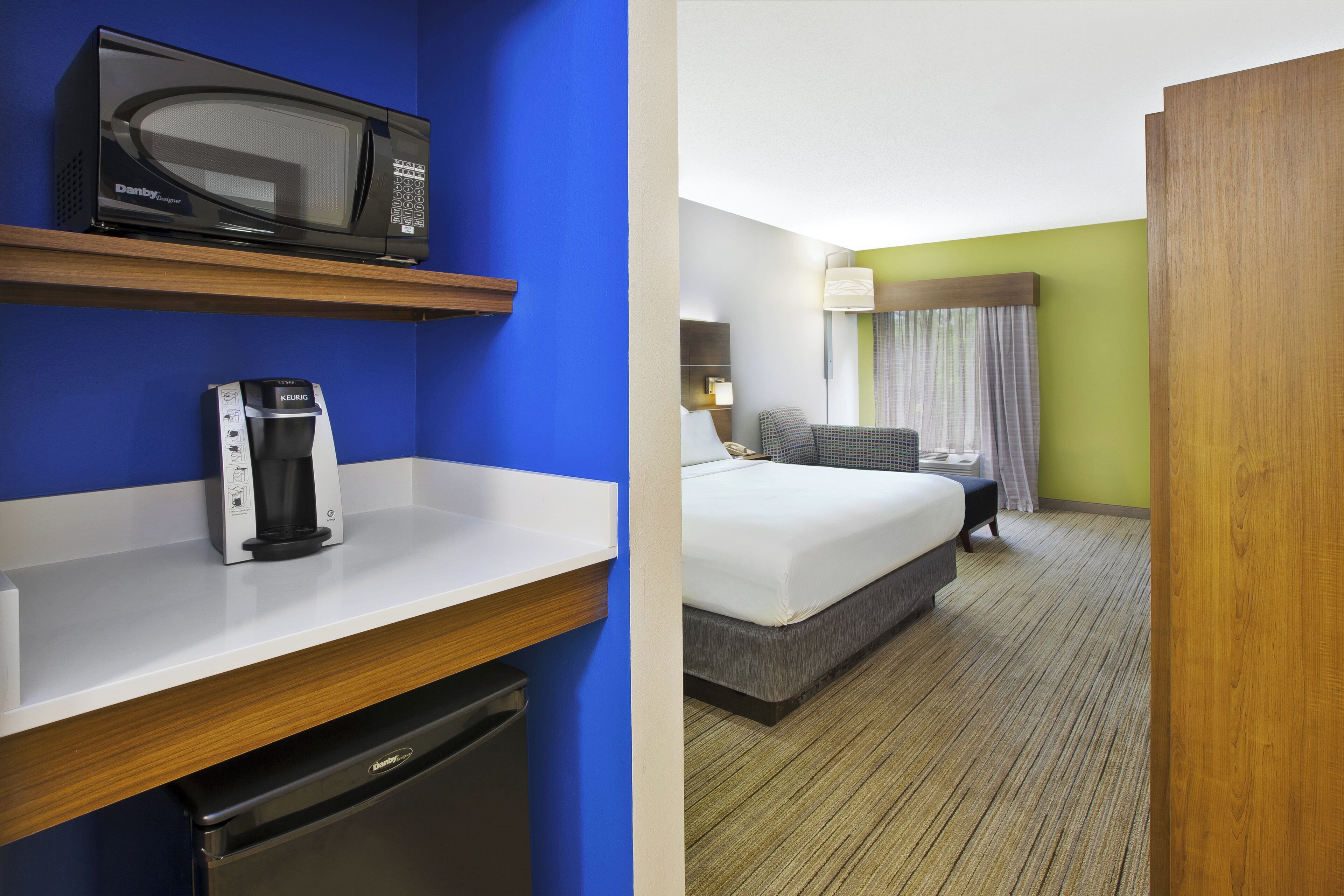 A hotel room with a bed, a desk with a microwave and a coffee maker, and a bathroom.