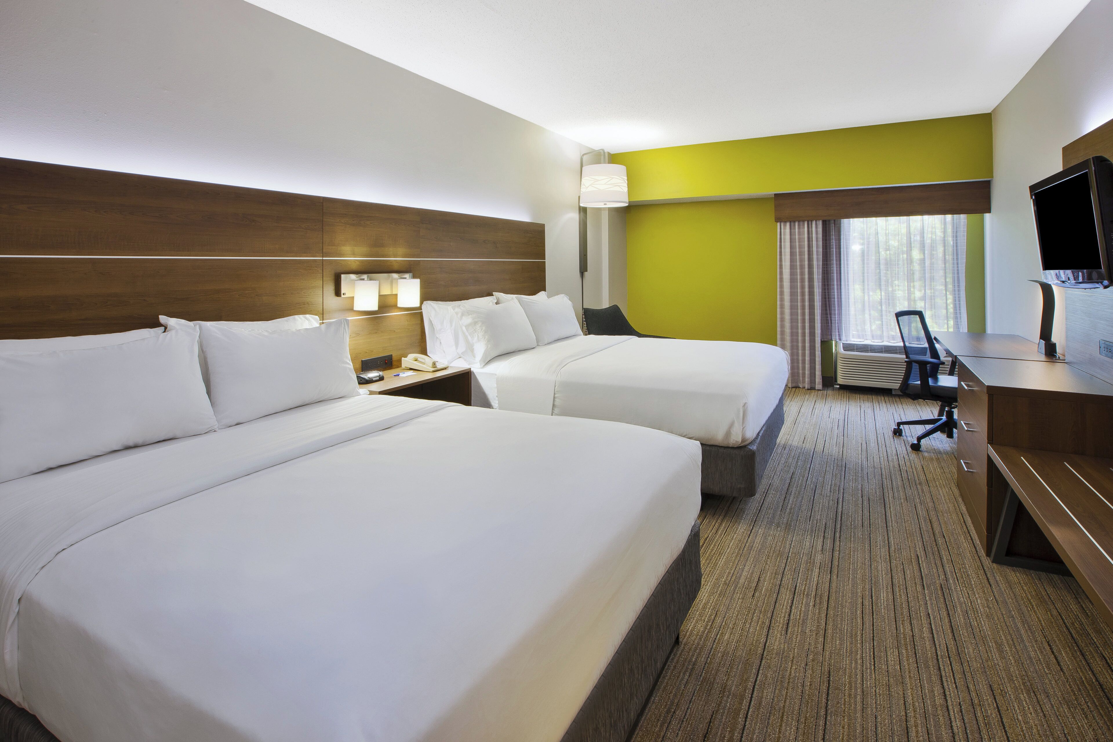 A hotel room with two beds, a desk, a chair, a television, and a window with curtains.
