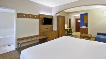 Habitación de hotel con cama, escritorio con silla, televisor montado en la pared, armario y baño visible a través de un arco.