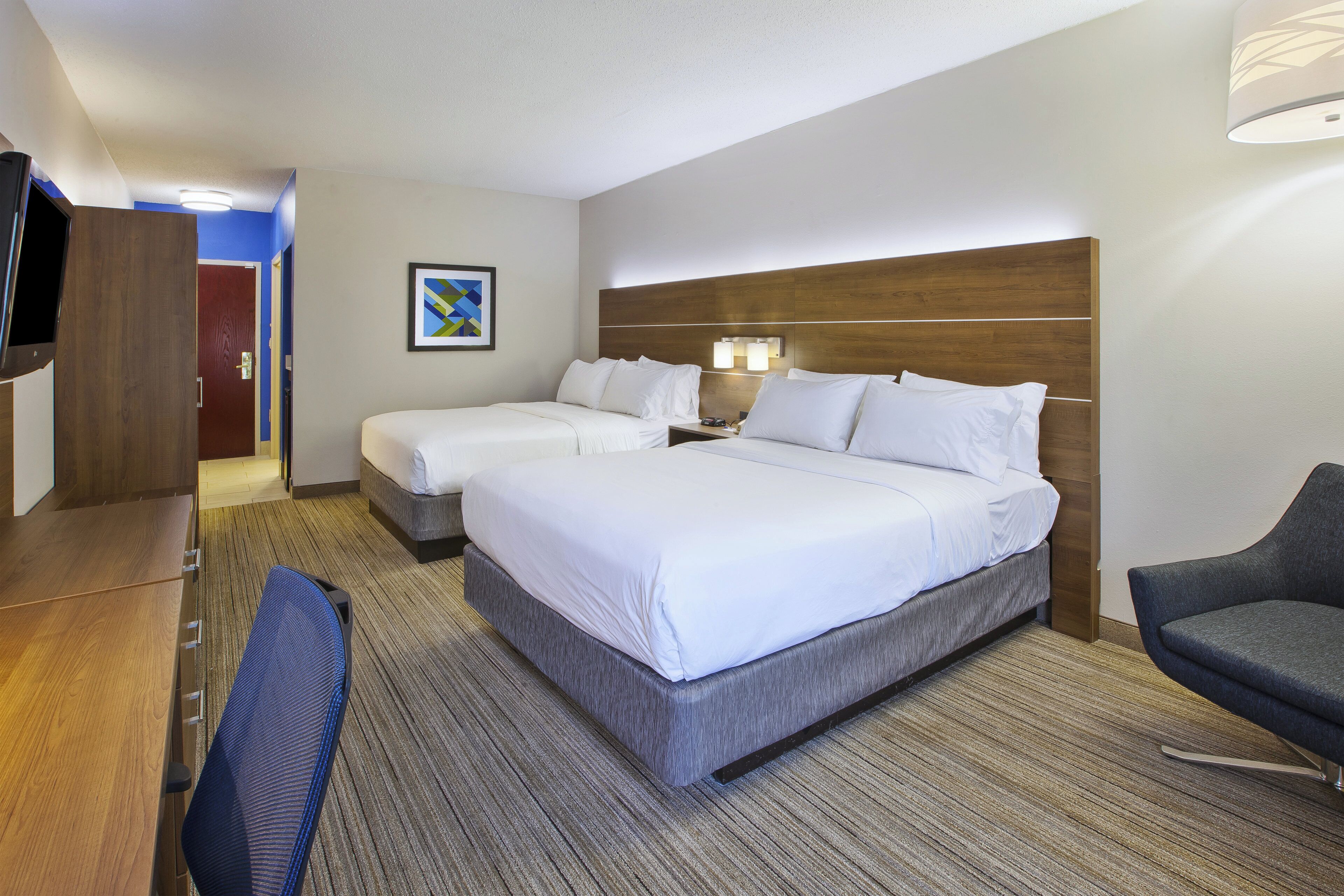 A hotel room with two beds, a desk, a chair, and a TV.
