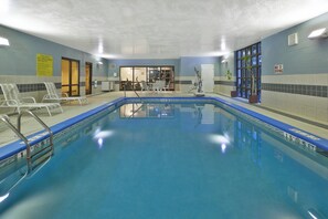 An indoor swimming pool with clear water, a lifeguard chair, and a pool rule sign.