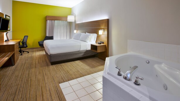 A hotel room with a bed, a desk, a chair, a desk lamp, a TV, a bathroom with a bathtub, and a shower.