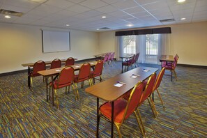 A conference room with a long table, multiple chairs, a projector screen, and a large window with curtains.