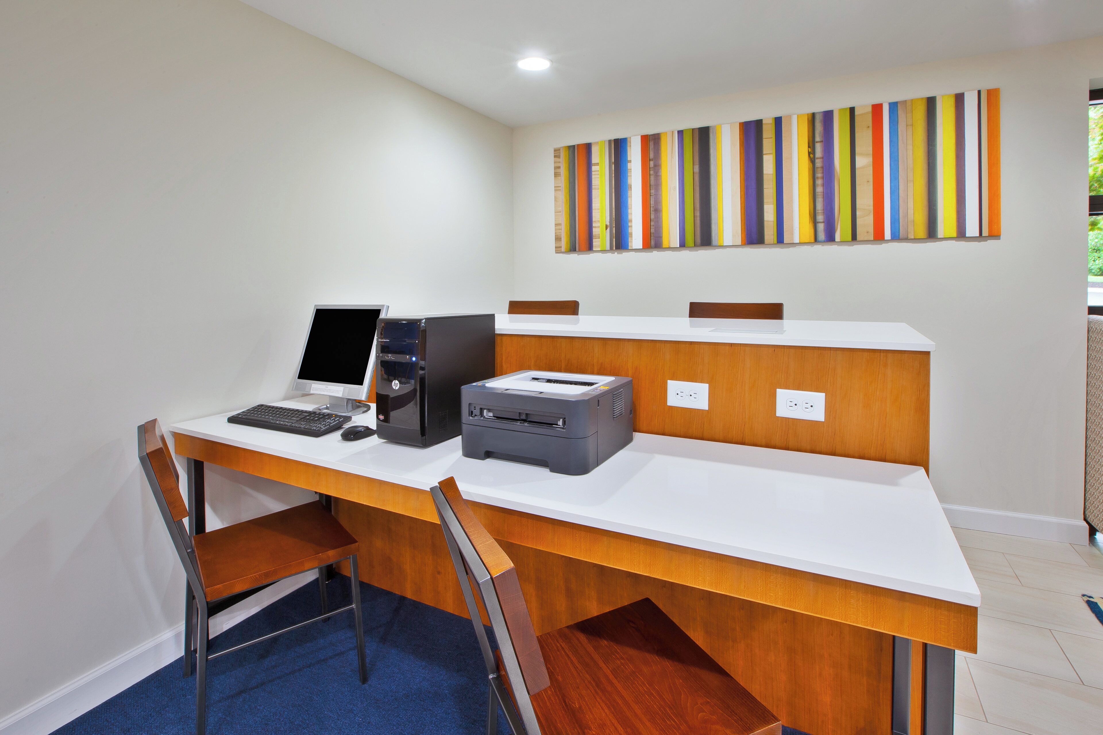 A modern office space with a desk, computer, printer, and a colorful abstract painting on the wall.