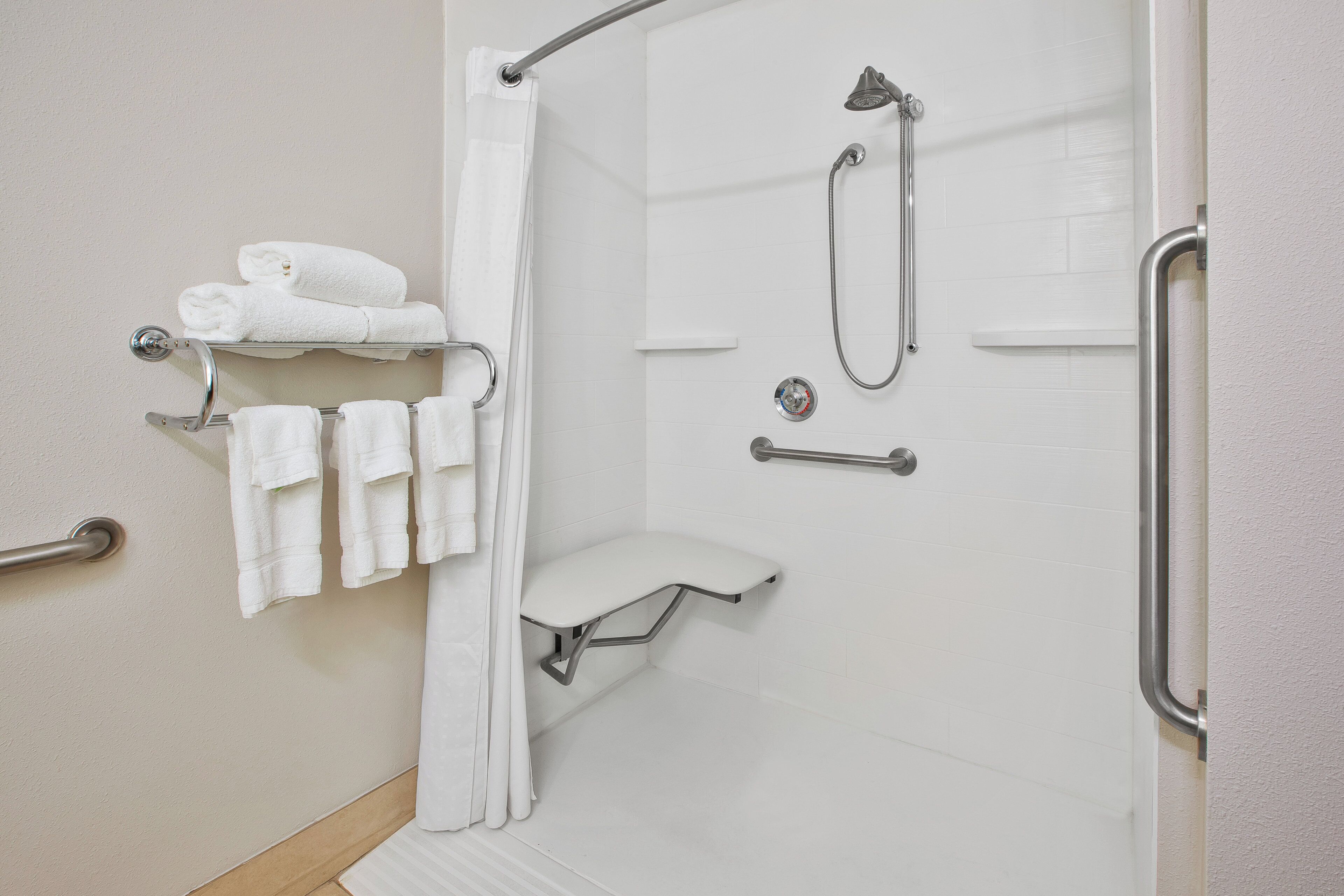 A shower area with a grab bar, a towel rack with towels, and a shower control panel.