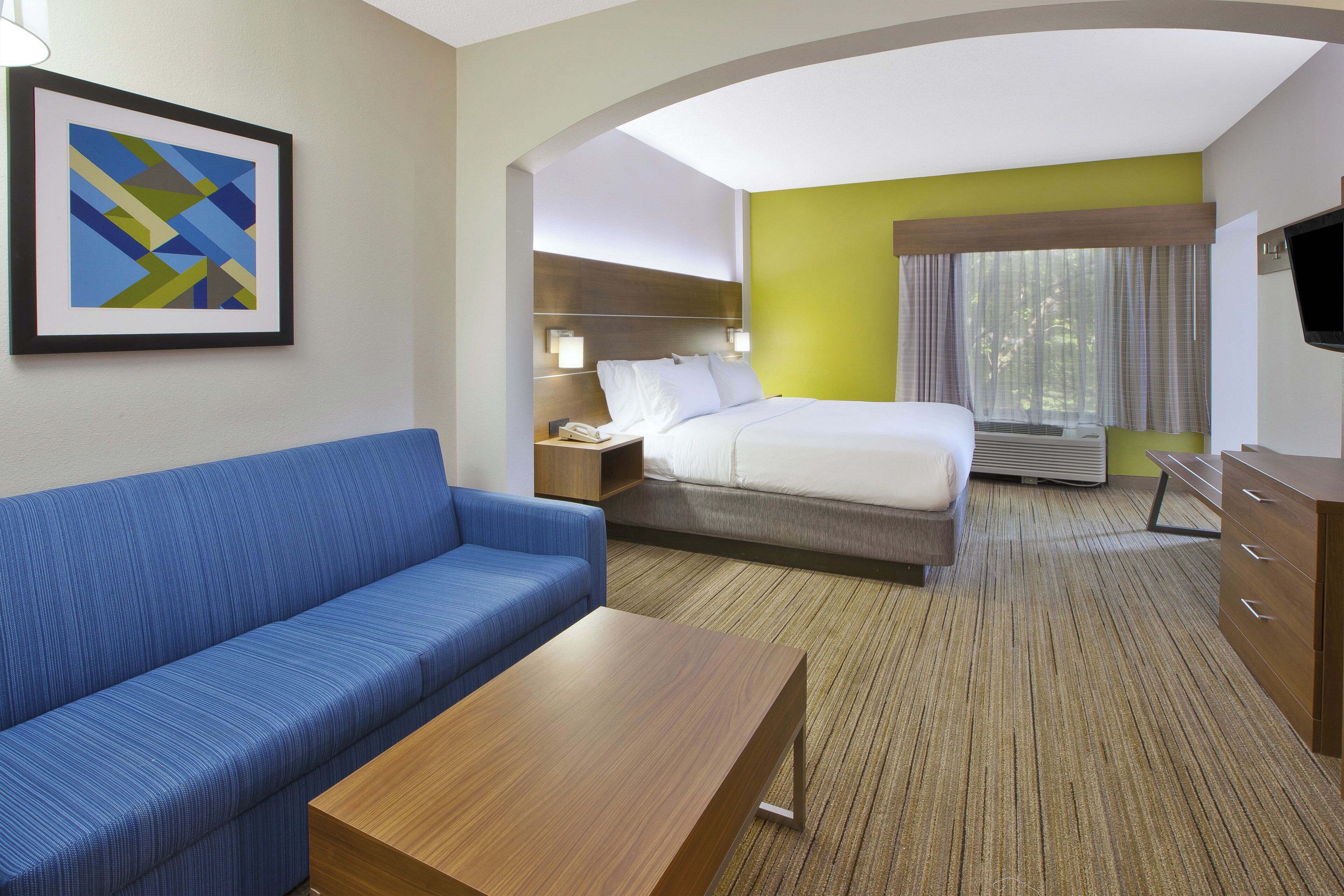 Habitación de hotel con cama, sofá, escritorio, televisión y un cuadro en la pared.