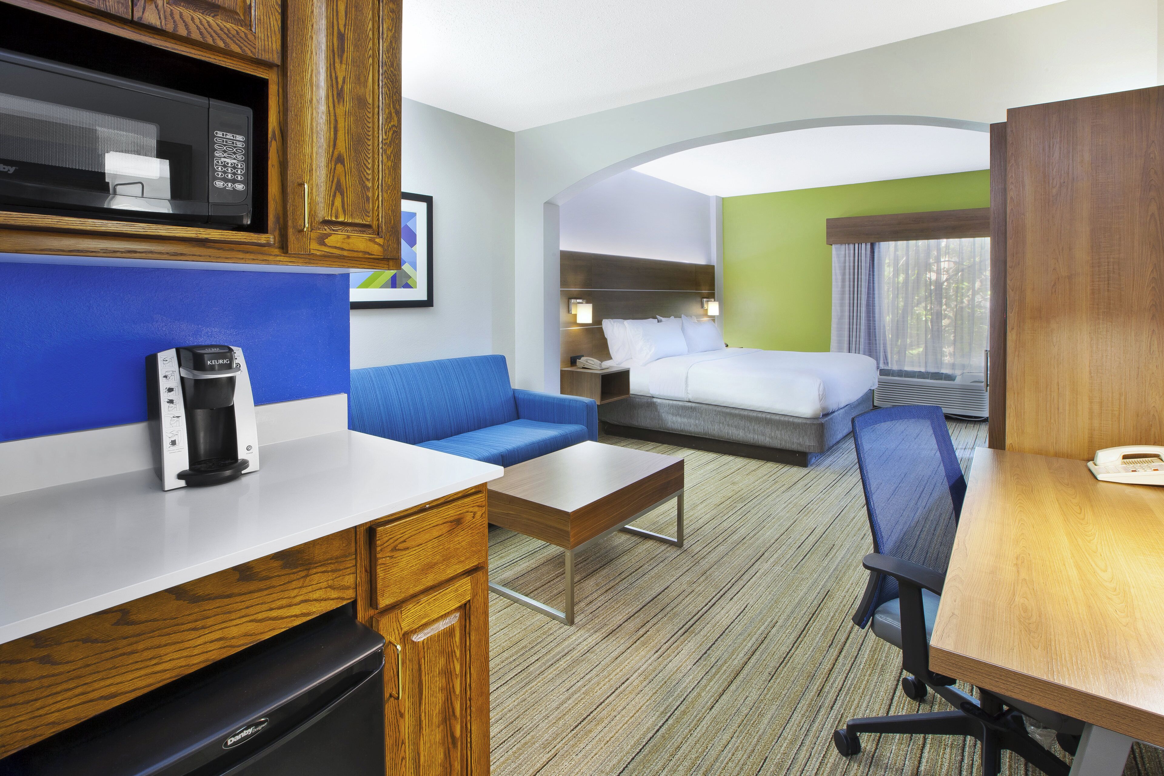 Habitación de hotel con kitchenette, cama, zona de estar y escritorio.