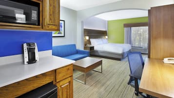 Habitación de hotel con kitchenette, cama, zona de estar y escritorio.