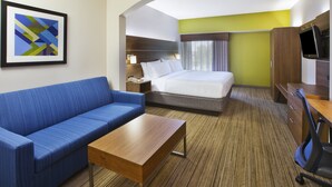 A hotel room with a bed, a blue sofa, a wooden table, a desk with a chair, and a TV.