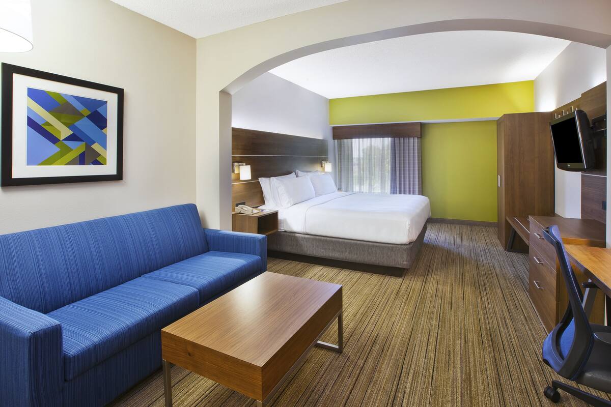 A hotel room with a bed, a blue sofa, a wooden table, a desk with a chair, and a TV.