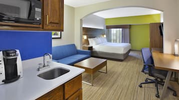 A hotel room with a kitchenette, a bed, a sofa, a desk, and a TV.