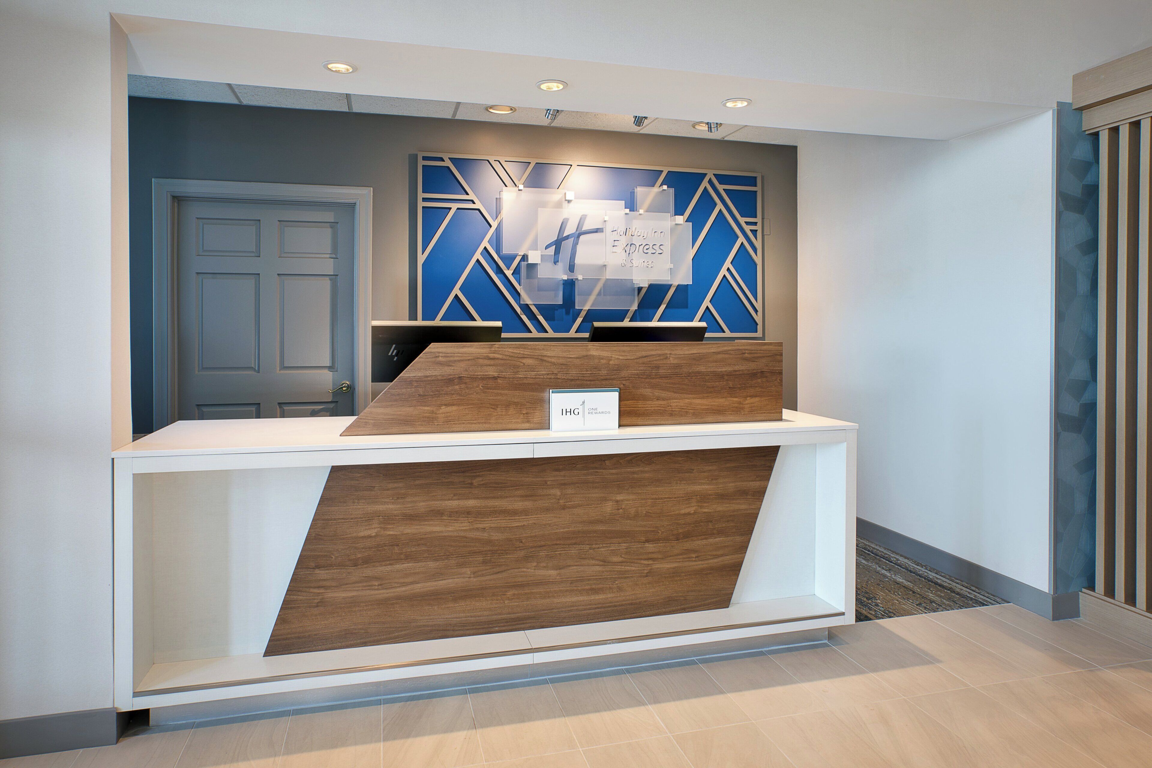Una reception dal design moderno, con uno schermo digitale e un cartello che indica 'Holiday Inn Express & Suites'.