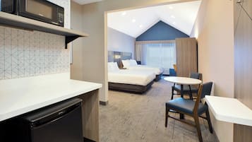 Quarto de hotel compacto com cozinha compacta, uma cama, um pequeno espaço de refeições e um banheiro.