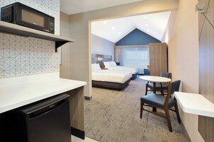A compact hotel room with a kitchenette, a bed, a small dining area, and a bathroom.