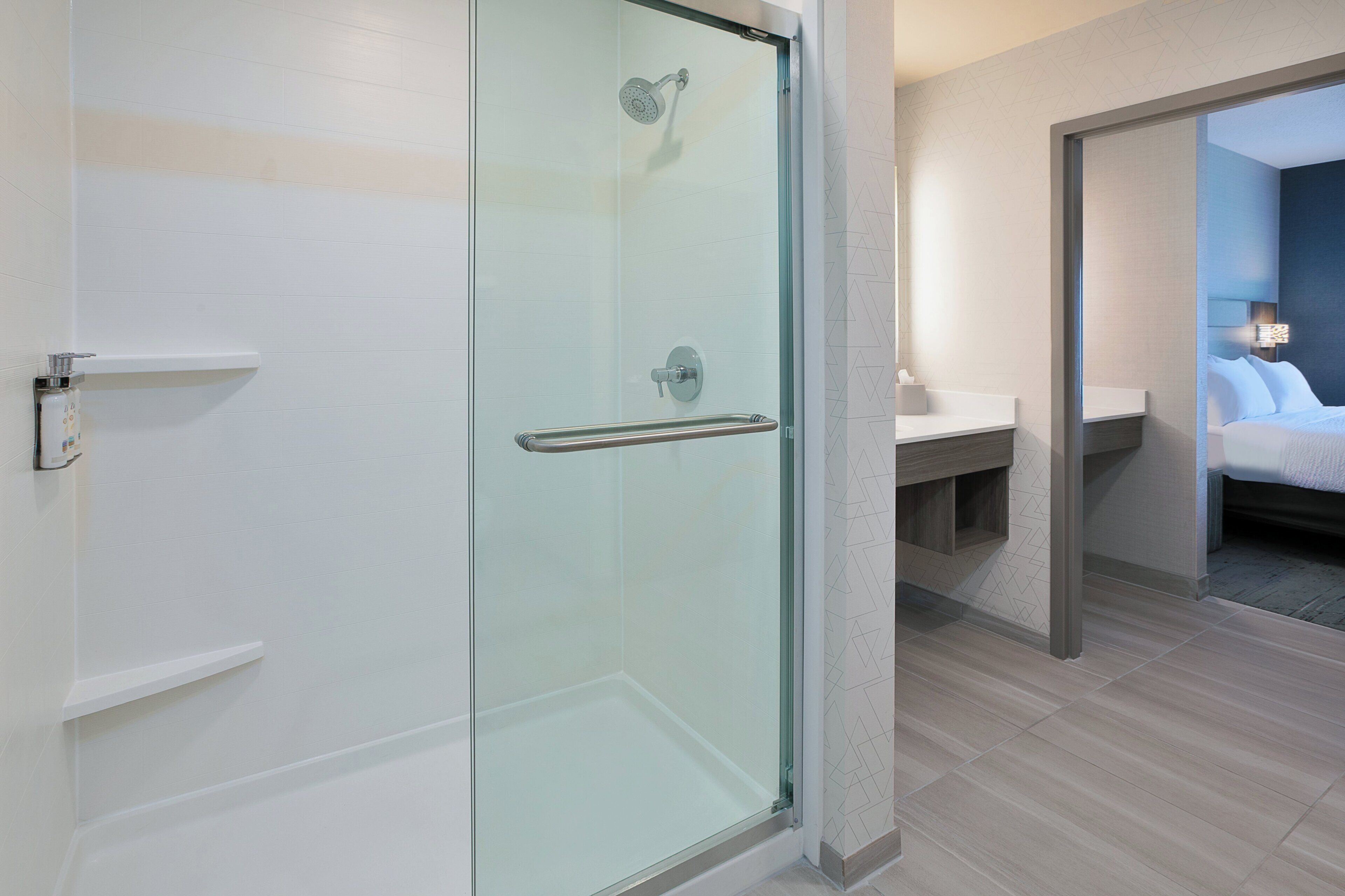 A modern bathroom with a glass shower enclosure, a white sink, and a bed with a nightstand.