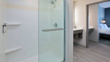 A modern bathroom with a glass shower enclosure, a white sink, and a bed with a nightstand.