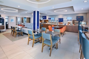Un restaurante moderno de hotel con varias zonas de estar, incluyendo una mesa central rodeada de sillas y un área de descanso separada con un sofá y sillas.