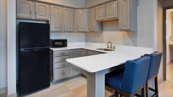A modern kitchen with a black refrigerator, a microwave, and a sink. There are light-colored cabinets and a white countertop.