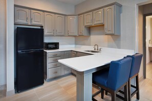 A modern kitchen with a black refrigerator, a microwave, and a sink. There are light-colored cabinets and a white countertop.