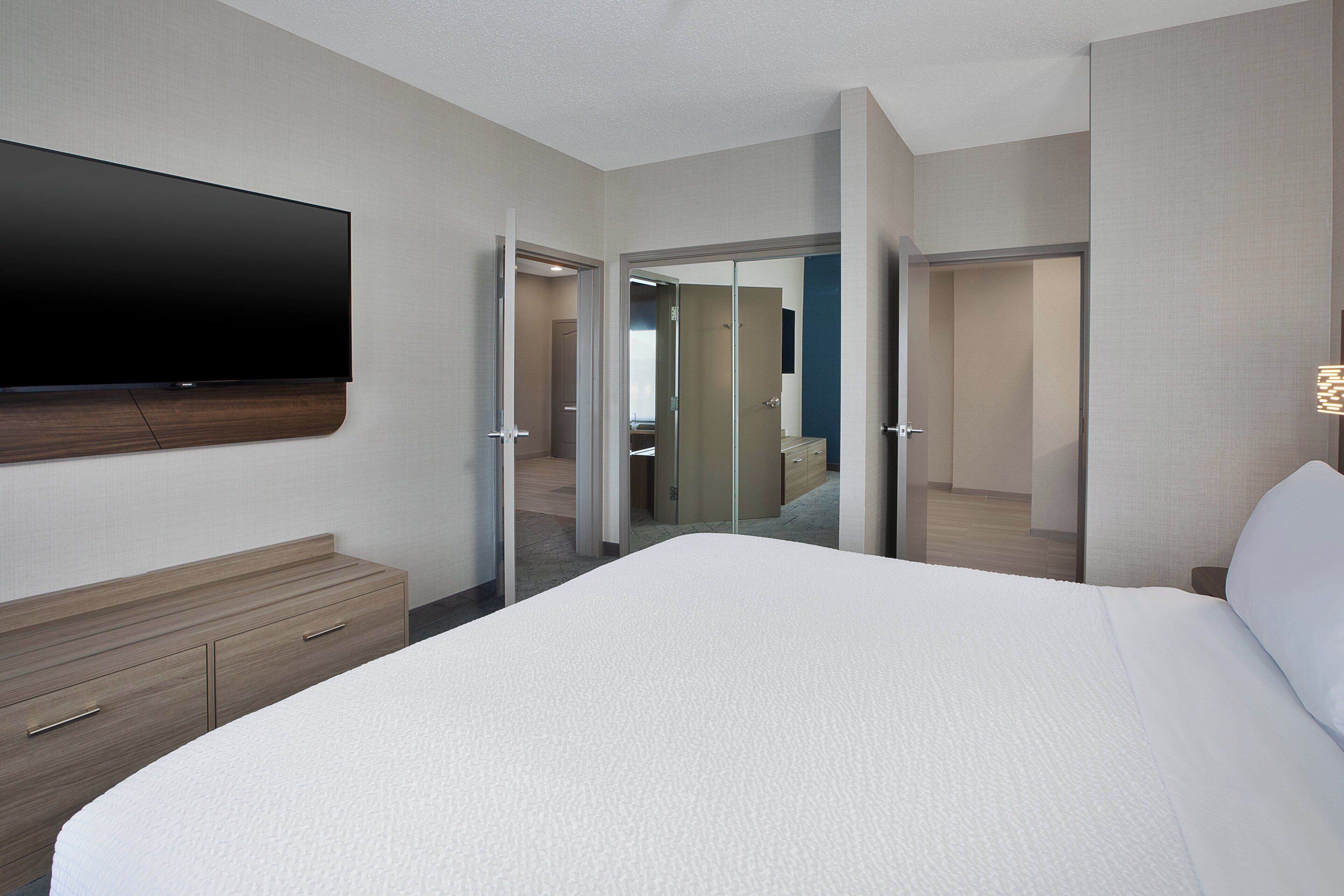 A hotel room with a bed, a TV mounted on the wall, a wooden dresser, and a mirror.