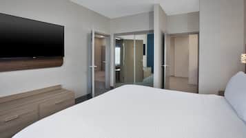 A hotel room with a bed, a TV mounted on the wall, a wooden dresser, and a mirror.